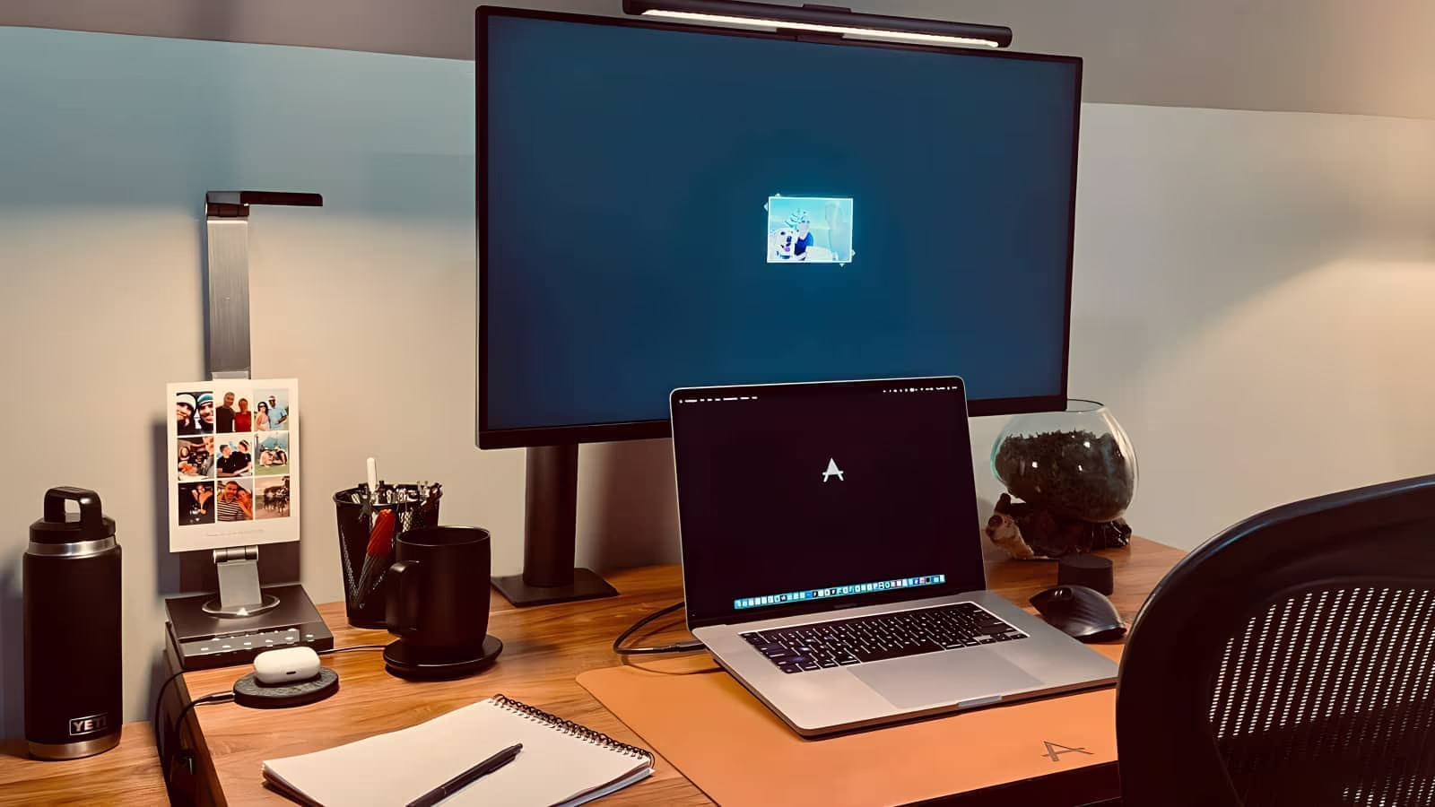 A neatly arranged workspace on a desk with a laptop, notebook, pen, glasses, and a plant